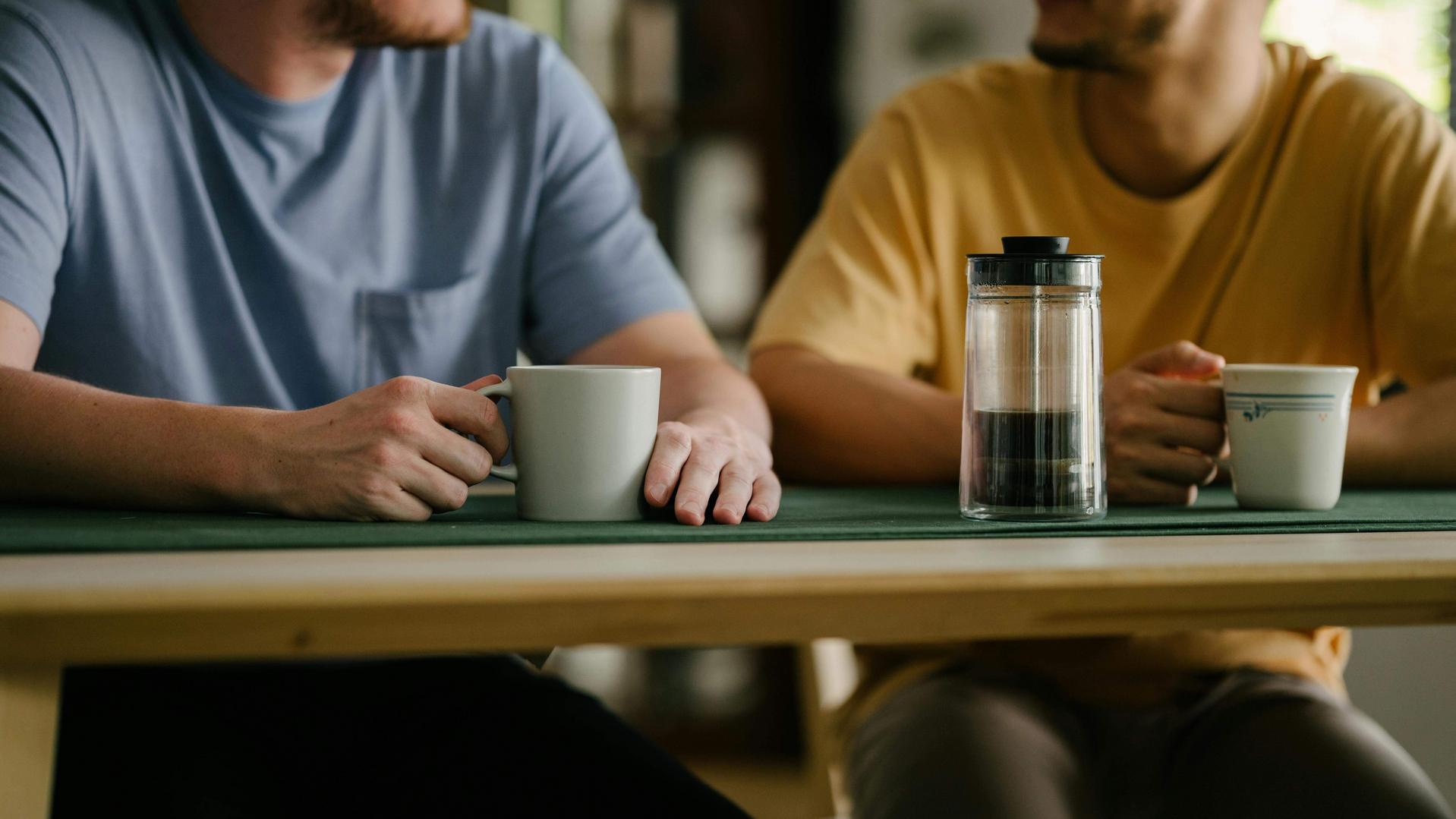 Nahaufnahme von 2 M&auml;nnern mit Kaffee am Esstisch