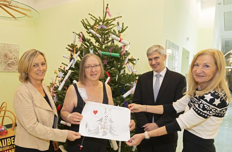 vier Personen halten vor einem Weihnachtsbaum eine Kinderzeichung