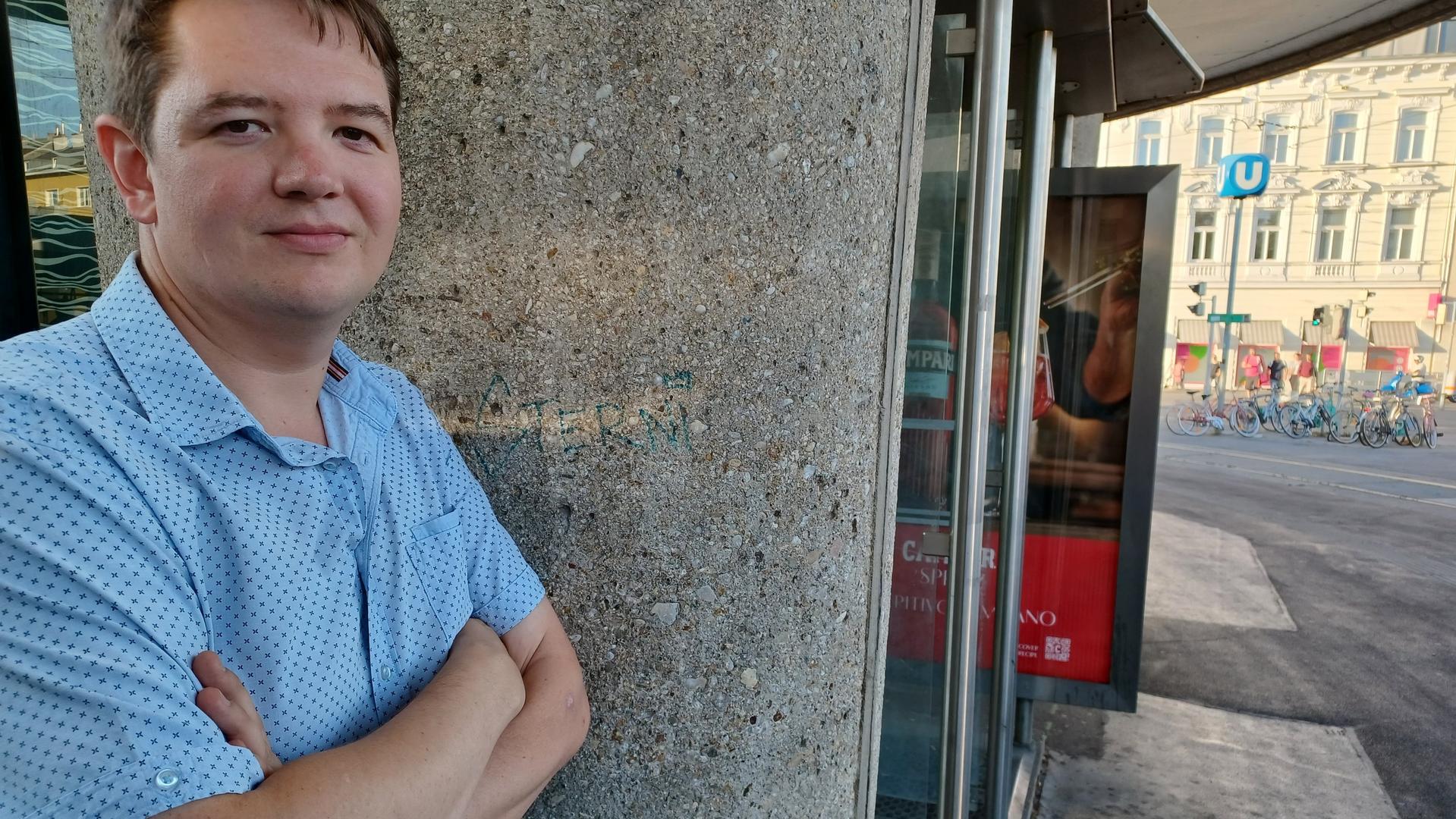 Lukas steht mit verschränkten Armen und Blick in die Kamera an eine Betonsäule gelehnt