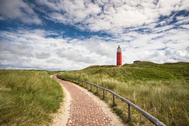 gepflasterter Weg durch Wiese f&uuml;hrt zu einem Leuchtturm auf H&uuml;gel
