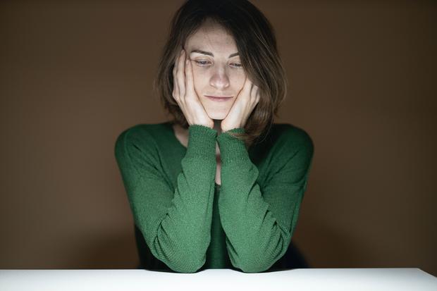 Frau in gr&uuml;nem Pullover, den Kopf in die H&auml;nde gest&uuml;tzt