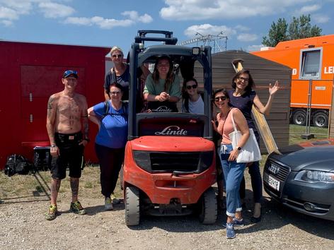 Mitarbeiterinnen der Krebshilfe Wien um Gabelstapler stehend bei Aufbauarbeiten für das Donauinselfest